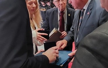 Mężczyzna wręcza dw&oacute;m osobom upominkowe medale i dyplomy.