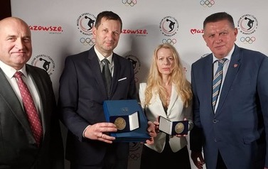 Trzech mężczyzn i kobieta pozują do zdjęcia. Kobieta i jeden mężczyzna trzymają w rękach medale.