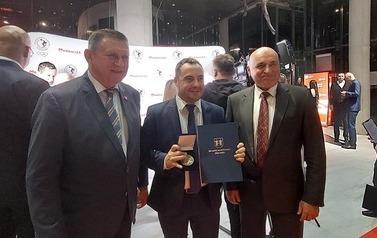 Trzech mężczyzn pozuje do zdjęcia, jeden z nich trzyma w rękach dyplom i medal