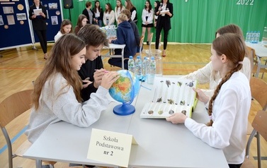 grupa os&oacute;b siedzi przy stole na kt&oacute;rym jest globus oraz butelki z wodą