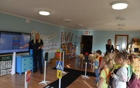 Strażniczka Miejska tlumaczy grupie dzieci co oznaczają znaki drogowe