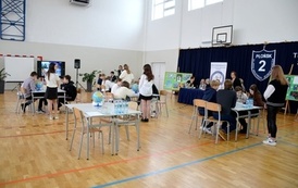 grupy os&oacute;b siedzą przy stołach w sali gimnastycznej