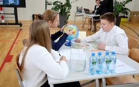 grupa os&oacute;b siedzi przy stole na kt&oacute;rym jest globus oraz butelki z wodą