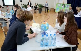 grupa os&oacute;b siedzi przy stole na kt&oacute;rym jest globus oraz butelki z wodą