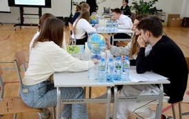 grupa os&oacute;b siedzi przy stole na kt&oacute;rym jest globus oraz butelki z wodą